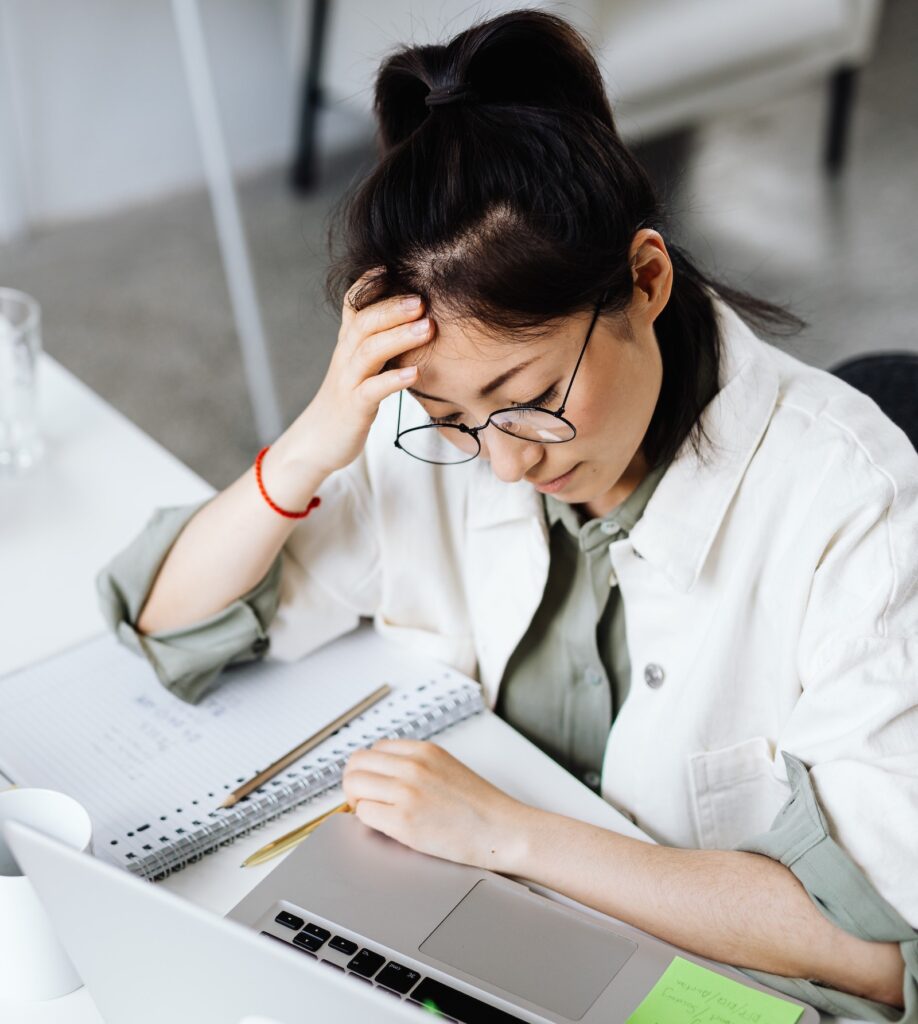 woman staring down at work on laptop with her hand on her head looking stressed